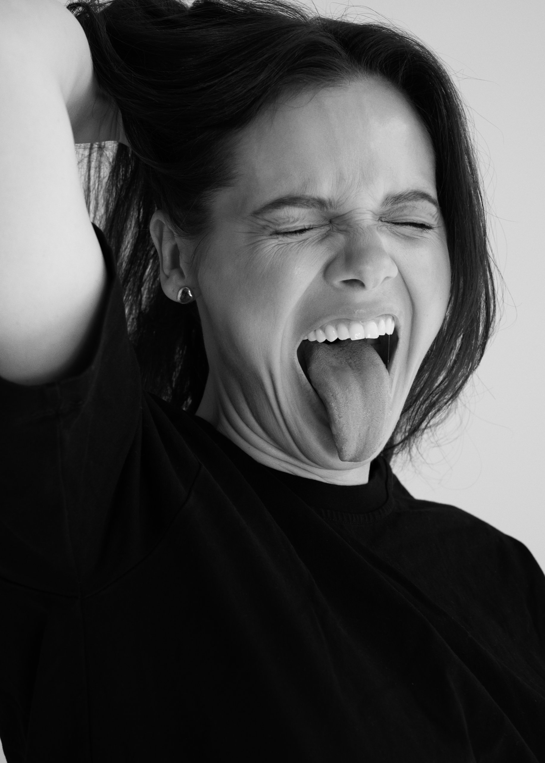Black-and-white portrait of Edyta Maksimowicz with closed eyes, tongue out and a hand in her hair