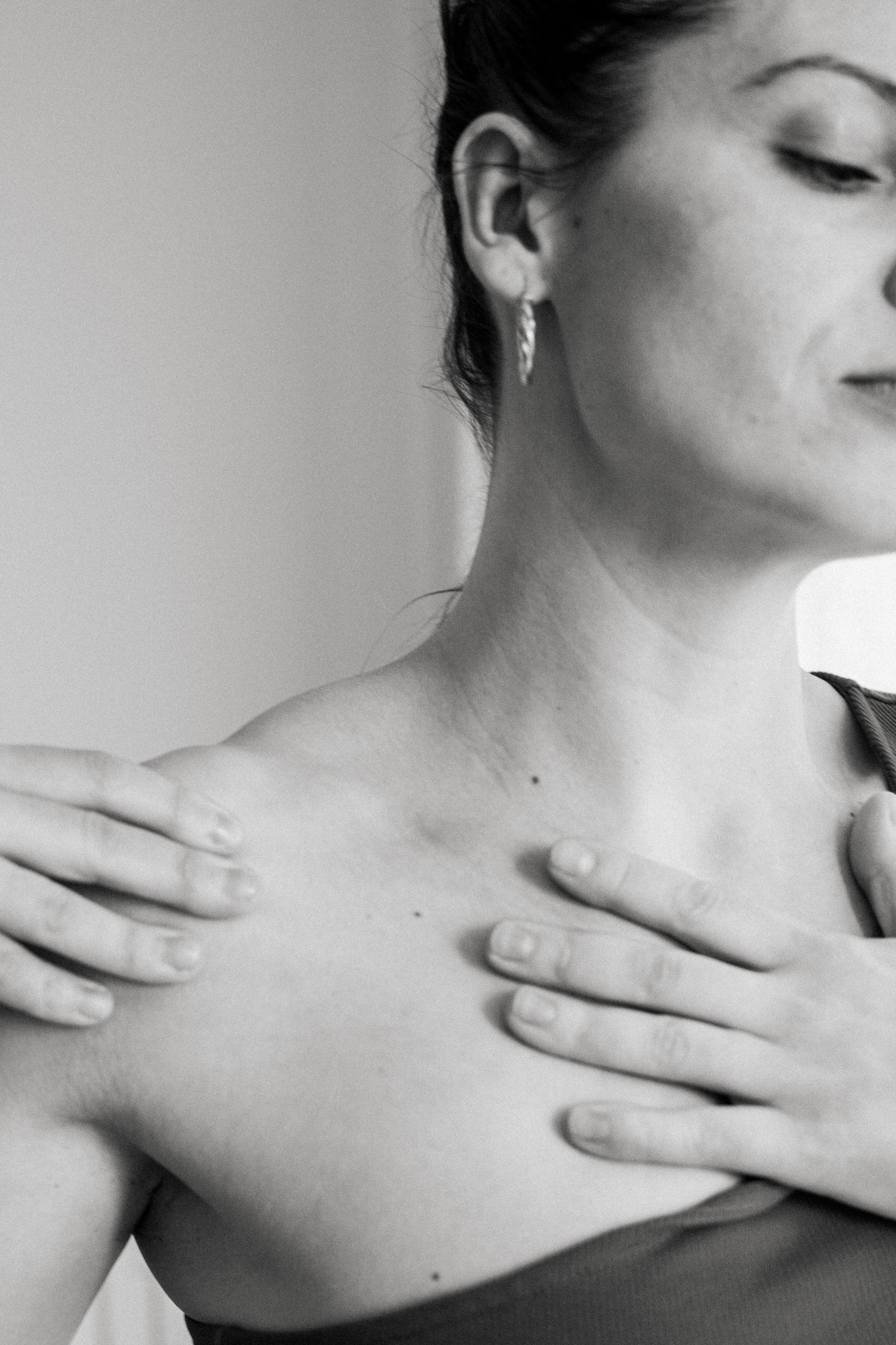 Black-and-white photograph of the neck and décolletage with hands near the collarbones