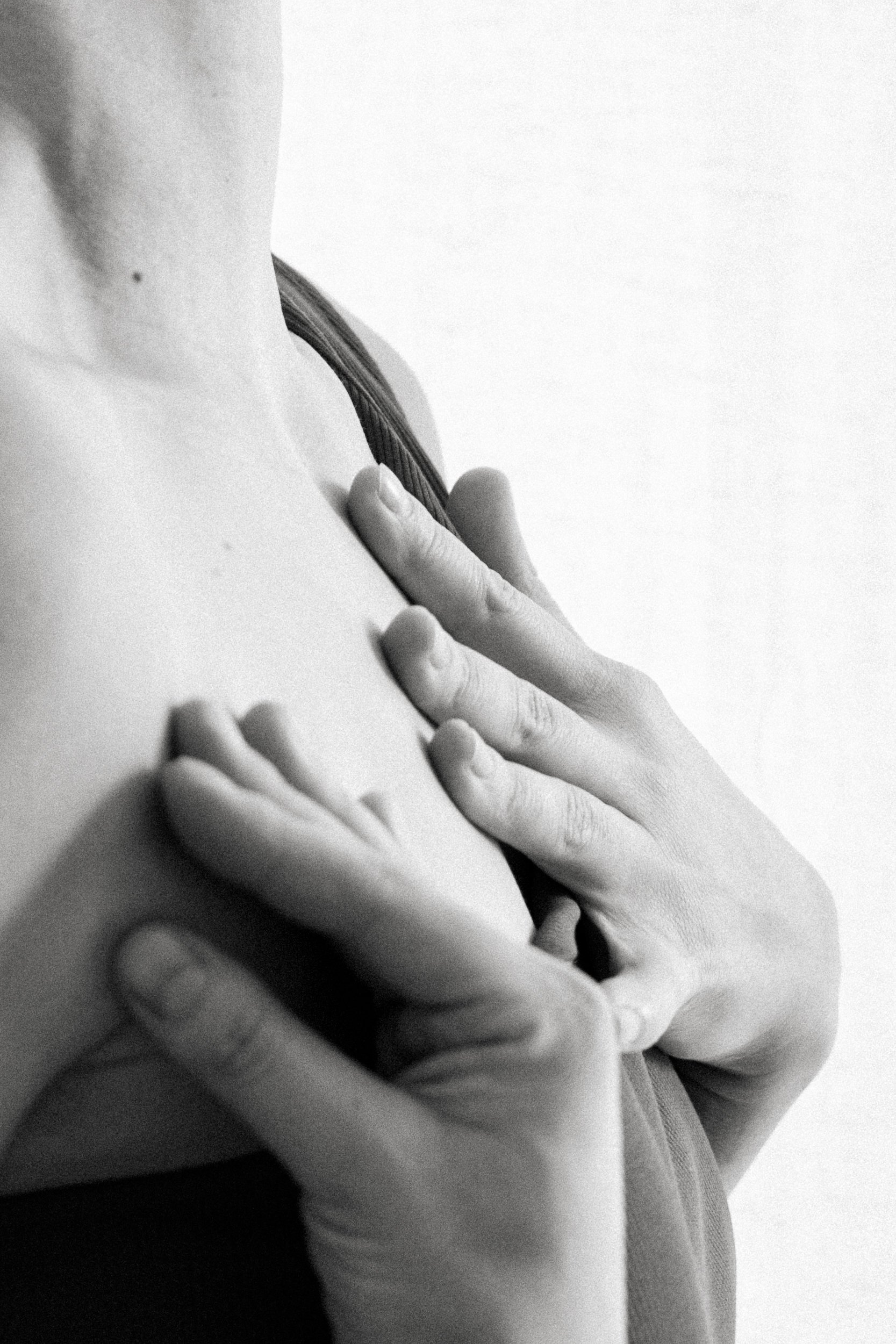 Black-and-white close-up of hands resting on the décolletage and neck